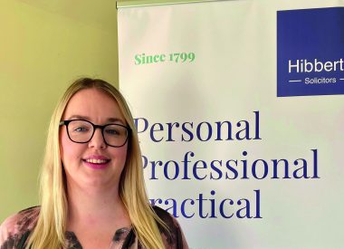 Michaela Warner standing in front of a Hibberts Solicitors Banner following her STEP qualification