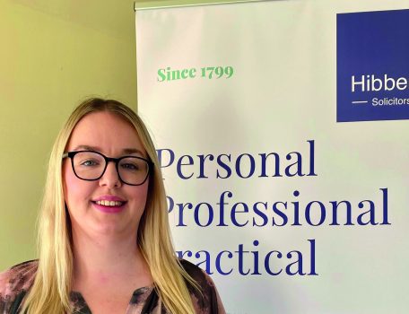 Michaela Warner standing in front of a Hibberts Solicitors Banner following her STEP qualification