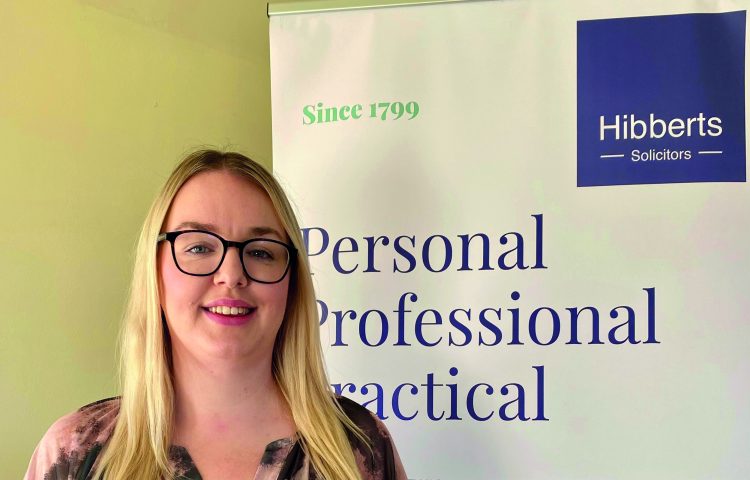 Michaela Warner standing in front of a Hibberts Solicitors Banner following her STEP qualification